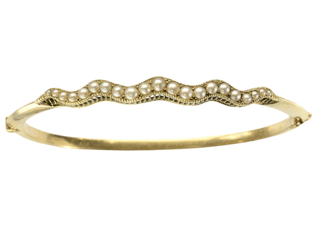 A thin gold c1900 Art Nouveau bracelet with a wavy line of pearls. Shown on white  background.