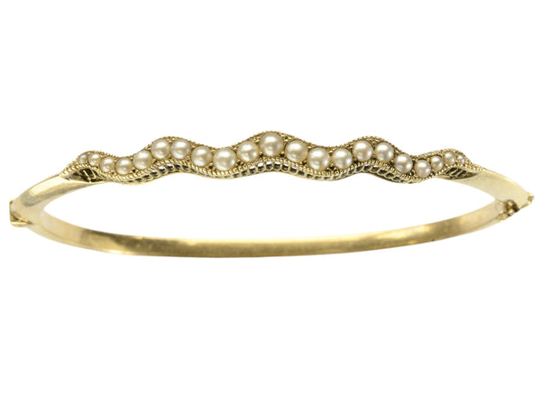 A thin gold c1900 Art Nouveau bracelet with a wavy line of pearls. Shown on white  background.