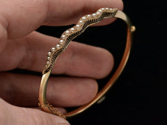 thumbnail of Angled view of thin gold c1900 Art Nouveau bracelet with a wavy line of pearls. Shown on in hand.