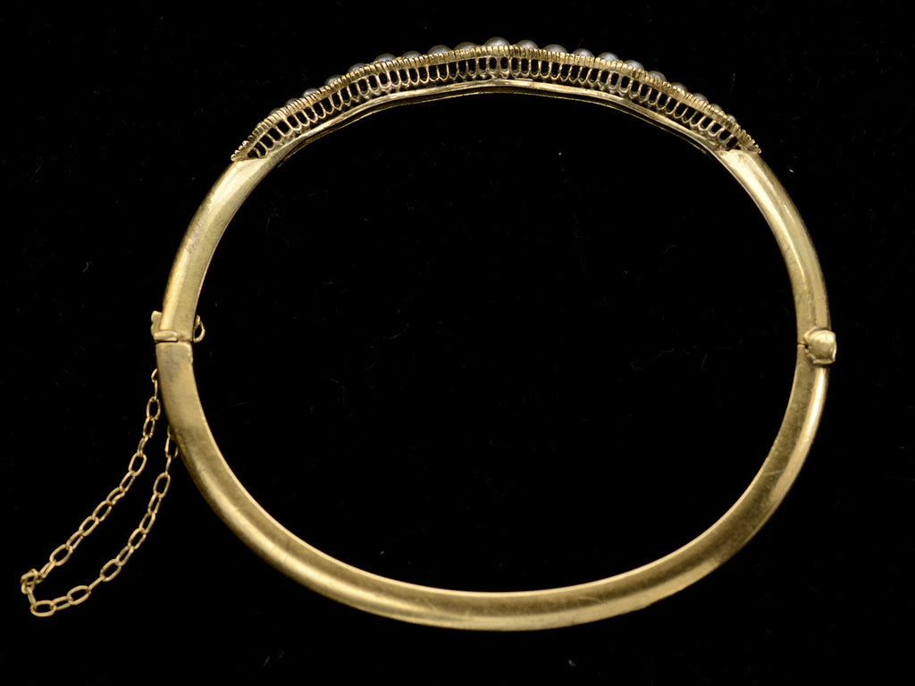 Side profile view of thin gold c1900 Art Nouveau bracelet with a wavy line of pearls. Shown on dark background.