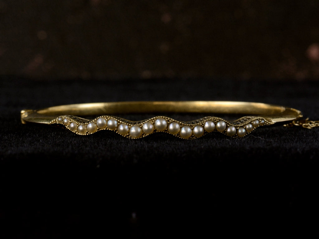 Front profile view of thin gold c1900 Art Nouveau bracelet with a wavy line of pearls. Shown on dark background.