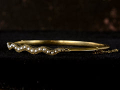 thumbnail of Right angled view of thin gold c1900 Art Nouveau bracelet with a wavy line of pearls. Shown on dark background.