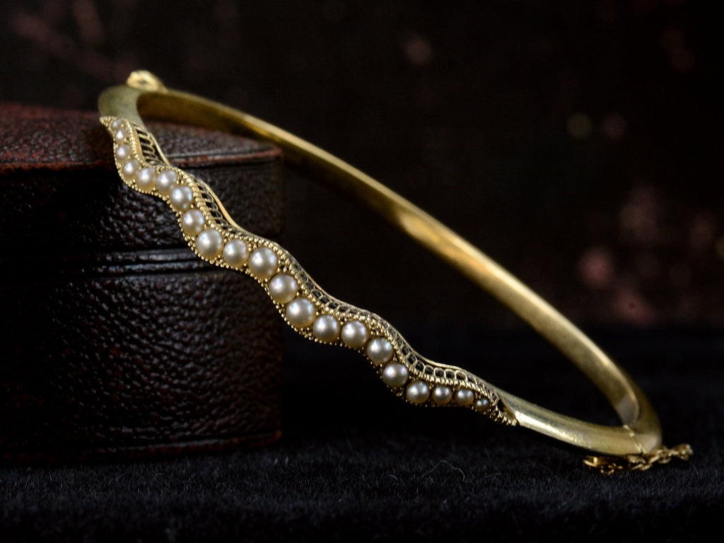 A thin gold c1900 Art Nouveau bracelet with a wavy line of pearls. Shown on propped up on an antique box.