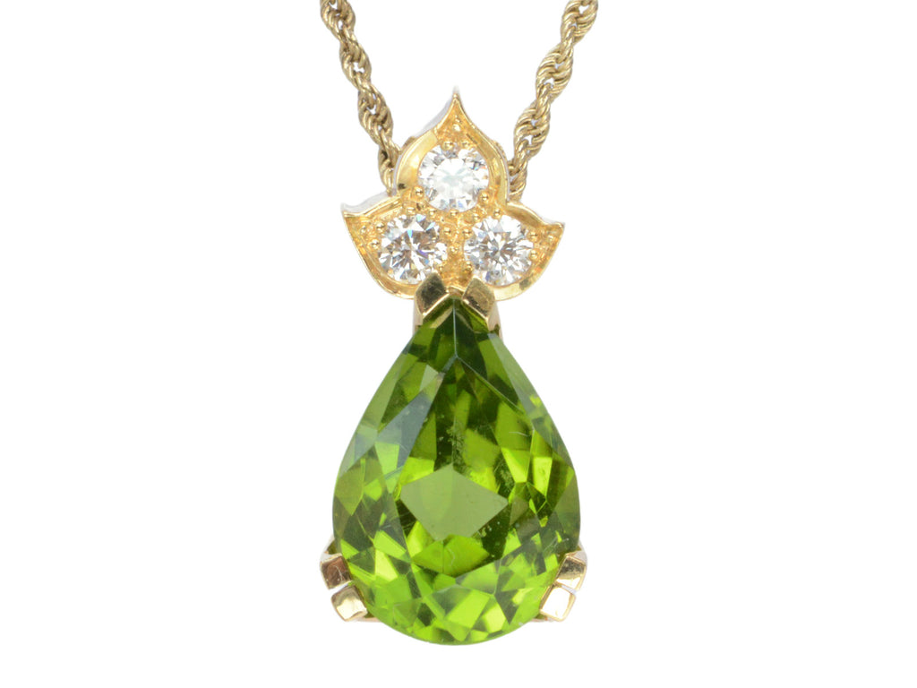 Detail of pear-shaped peridot set beneath three diamonds set in 18k yellow gold, shown on white background.