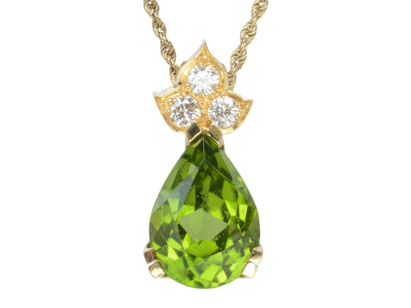 Detail of pear-shaped peridot set beneath three diamonds set in 18k yellow gold, shown on white background.