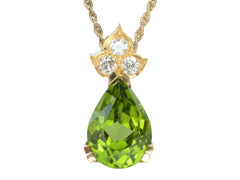 thumbnail of Detail of pear-shaped peridot set beneath three diamonds set in 18k yellow gold, shown on white background.