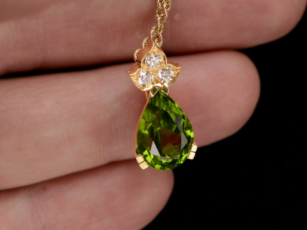 Detail of pear-shaped peridot set beneath three diamonds set in 18k yellow gold, shown held in hand