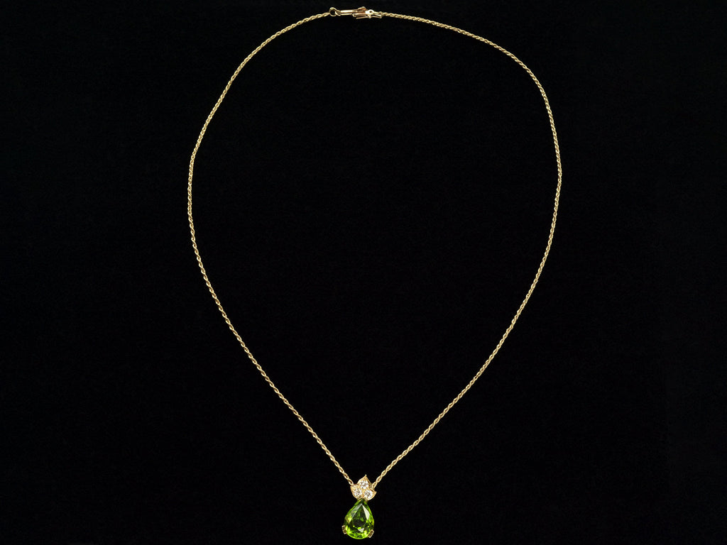 Pear-shaped peridot pendant set beneath three diamonds set in 18k yellow gold hanging on gold rope chain, shown on black background.