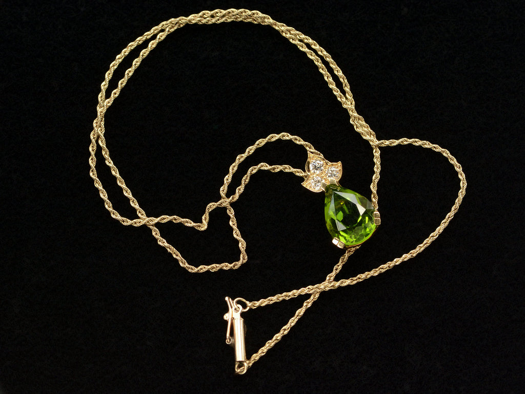 Detail chain and pear-shaped peridot set beneath three diamonds set in 18k yellow gold, shown on black background.