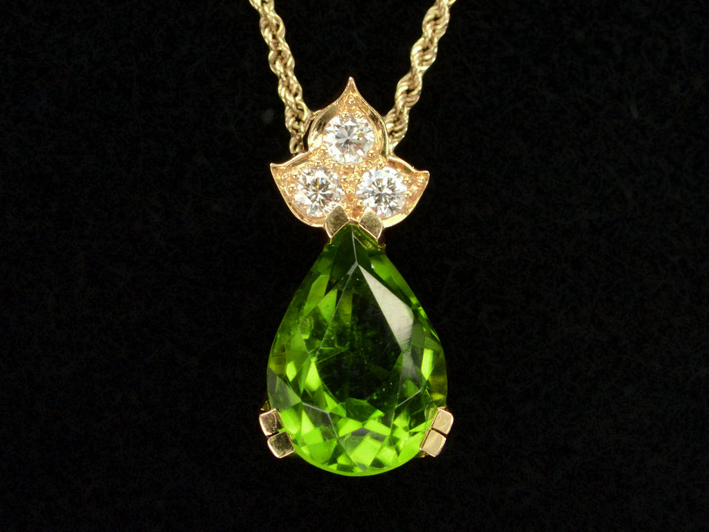 Detail of pear-shaped peridot set beneath three diamonds set in 18k yellow gold, shown on black background.