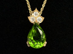 thumbnail of Detail of pear-shaped peridot set beneath three diamonds set in 18k yellow gold, shown on black background.