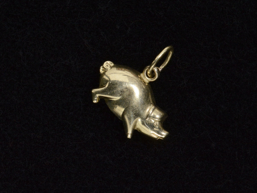 Gold pig charm on a black background, facing right