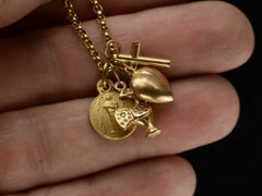 thumbnail of Detail of vintage 19k yellow gold Portuguese charm necklace with four charms: a devotional medallion of Christ, a rooster, a heart, and a cross. Shown held in hand.
