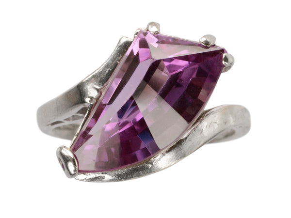 A white gold ring with wing shaped faceted purple stone, on white background.