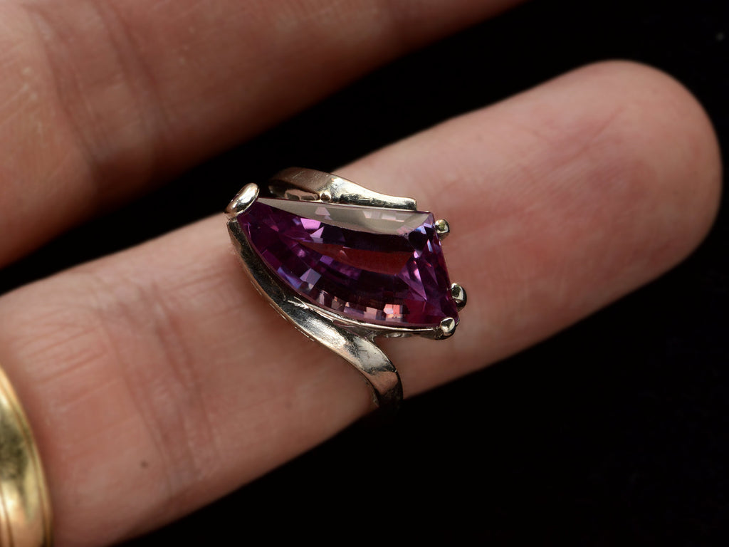 Front view of white gold ring with wing shaped faceted purple stone, on finger