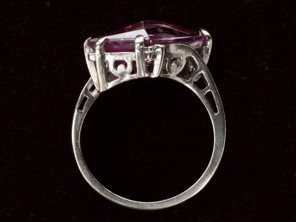 Side profile of white gold ring with wing shaped faceted purple stone, on black background.