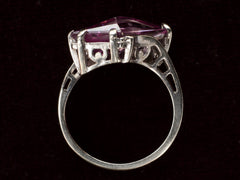 thumbnail of Side profile of white gold ring with wing shaped faceted purple stone, on black background.