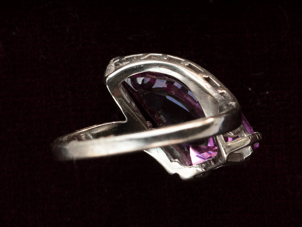 Inside view of white gold ring with wing shaped faceted purple stone, on black background.