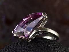 thumbnail of Angled view white gold ring with wing shaped faceted purple stone, on dark background.