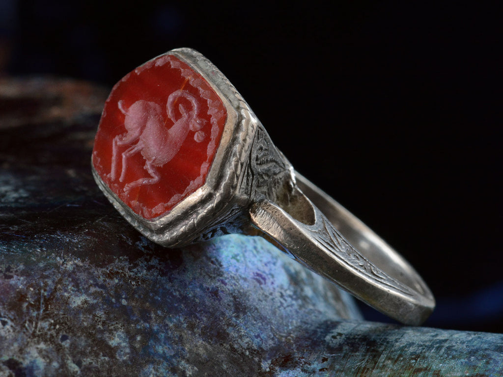 Angled front view of silver 19th century Persian carnelian intaglio ring with carved ram motif.  (shown on dark background)