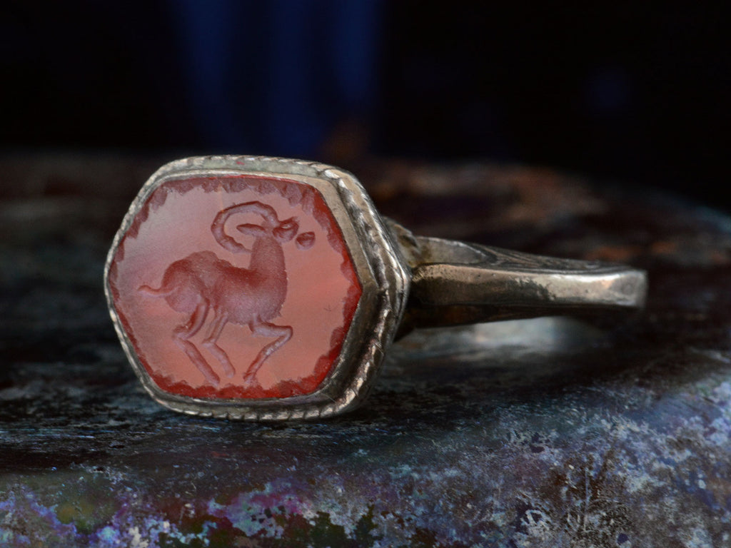 Angled front view of silver 19th century Persian carnelian intaglio ring with carved ram motif.  (shown on dark background)