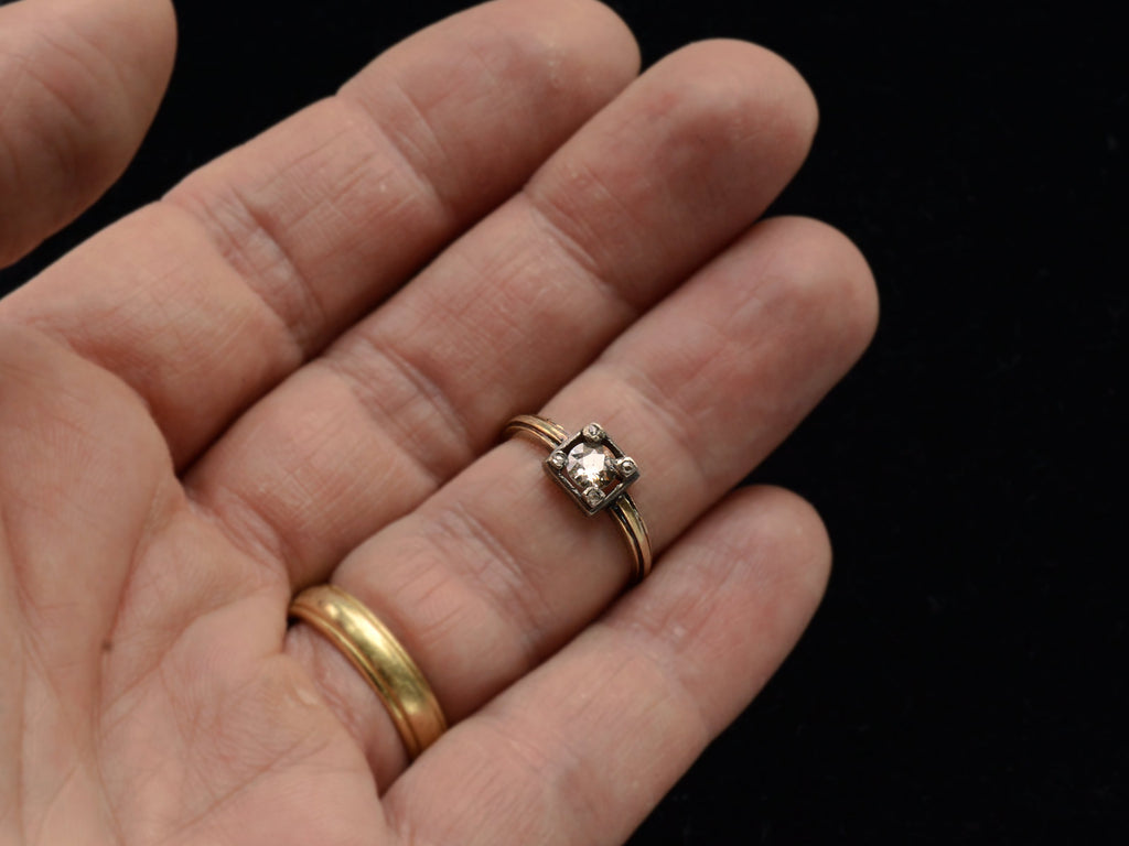 Antique silver-topped yellow gold ring with round diamond set on four prongs topped with tiny rose cut diamonds, shown on hand.