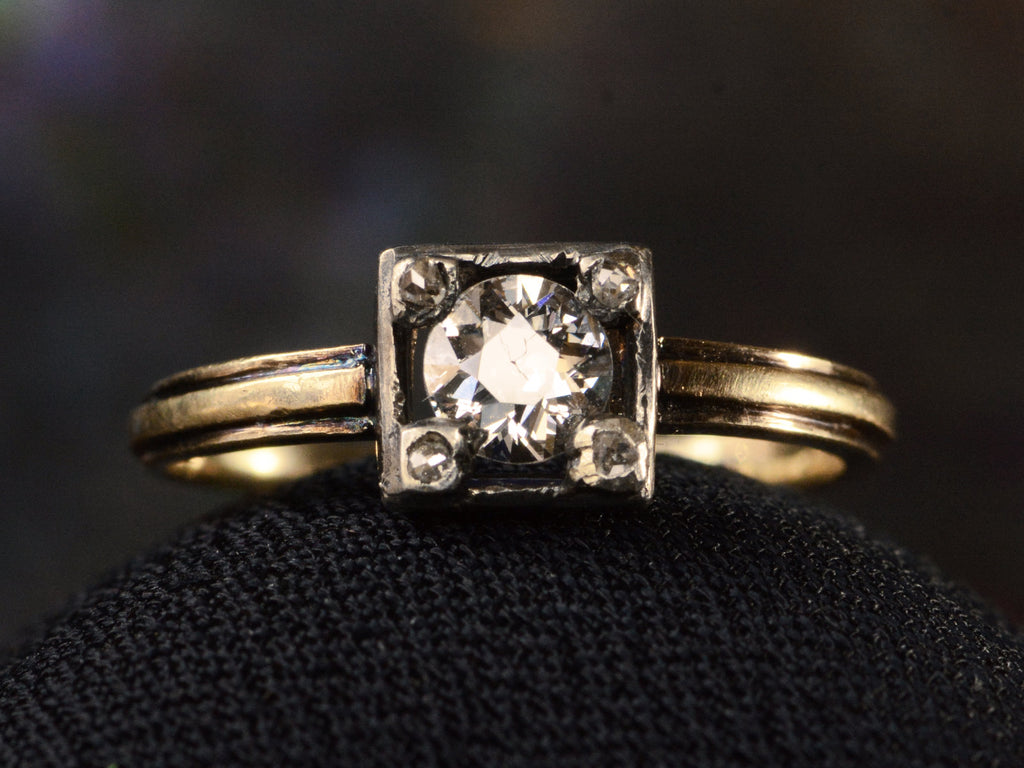 Front of silver-topped yellow gold ring with round diamond set on four prongs topped with tiny rose cut diamonds, shown on dark background.