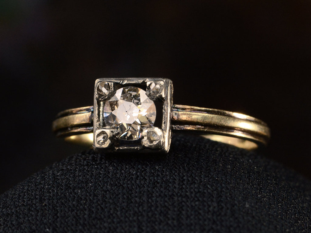 Angled view of silver-topped yellow gold ring with round diamond set on four prongs topped with tiny rose cut diamonds, shown on dark background.