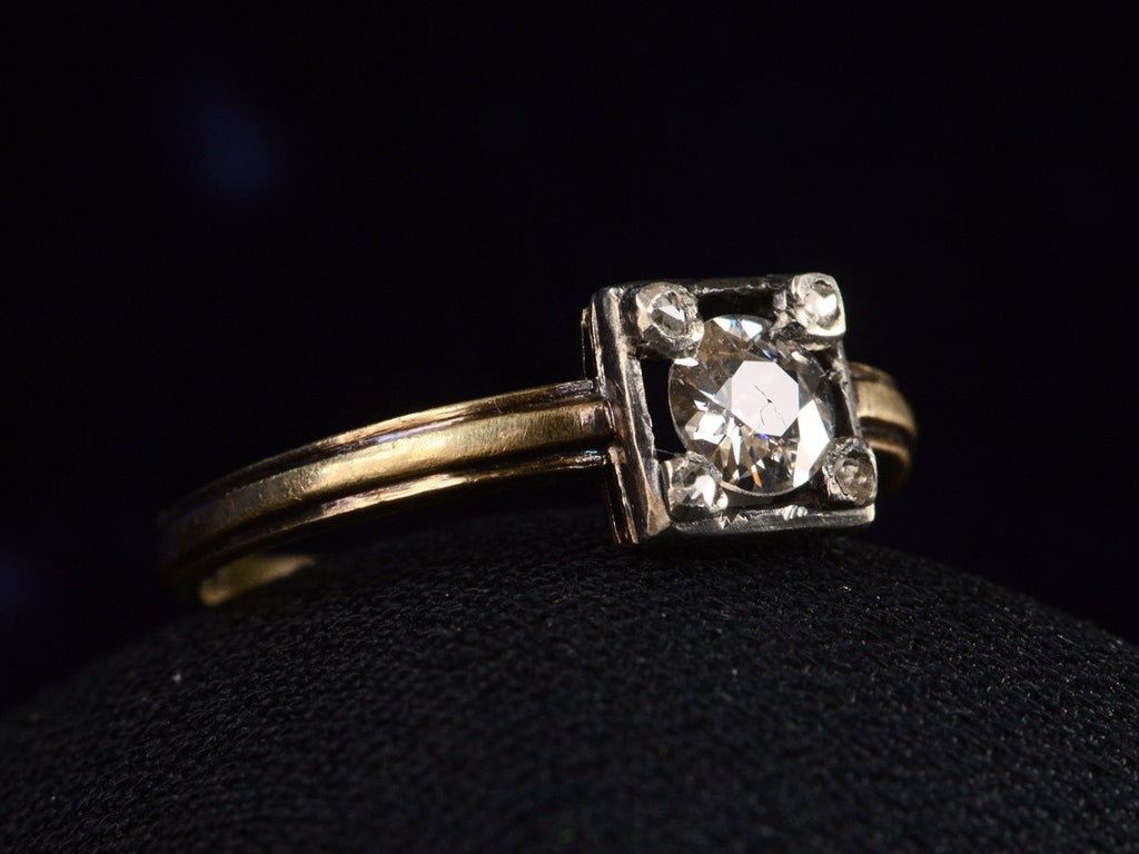 Side view of silver-topped yellow gold ring with round diamond set on four prongs topped with tiny rose cut diamonds, shown on dark background.