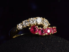 thumbnail of Angled view of c1970 Yellow Gold Ring with rows of pink rubies and white diamonds curling around each other. On dark background.