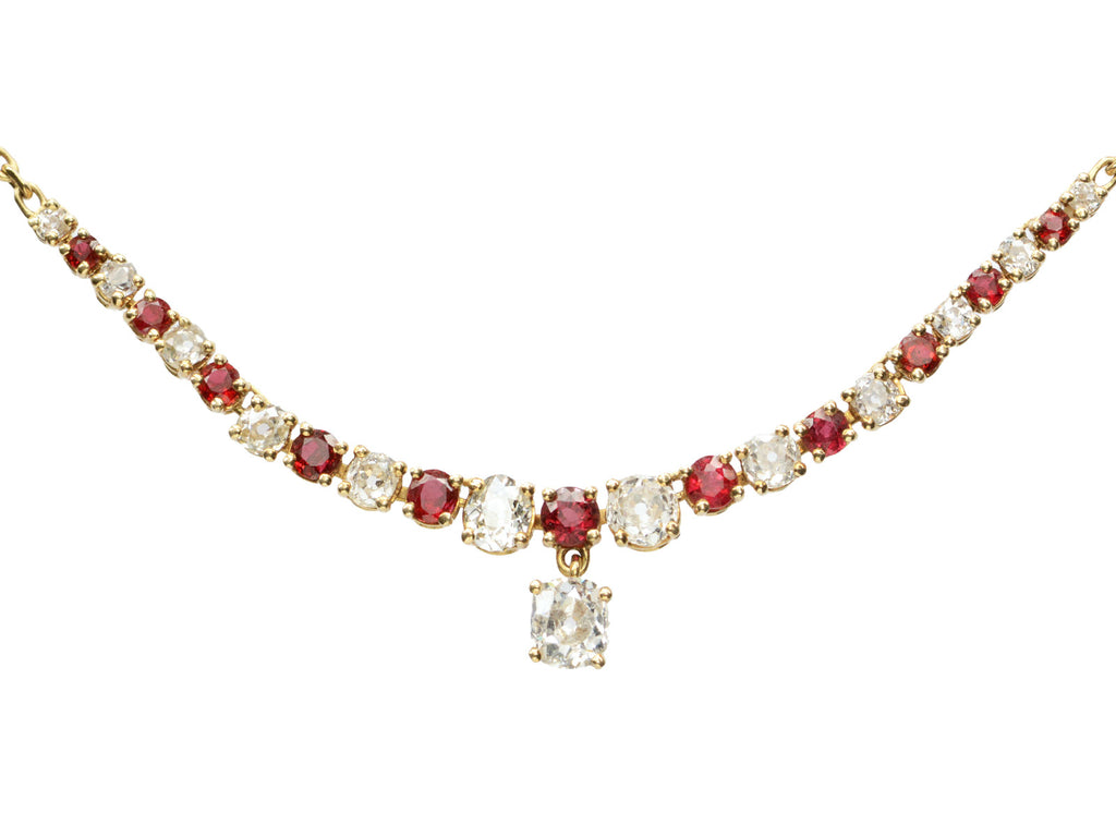 Close up on a vintage yellow gold necklace with alternating red rubies and old mine cut diamonds, shown on white background.