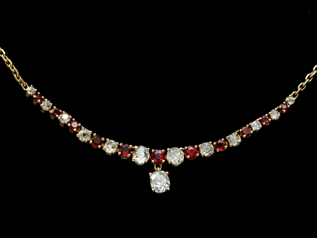 Close up on a vintage yellow gold necklace with alternating red rubies and old mine cut diamonds, shown on black background.