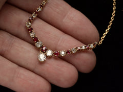 thumbnail of Close up on a vintage yellow gold necklace with alternating red rubies and old mine cut diamonds, shown held in hand
