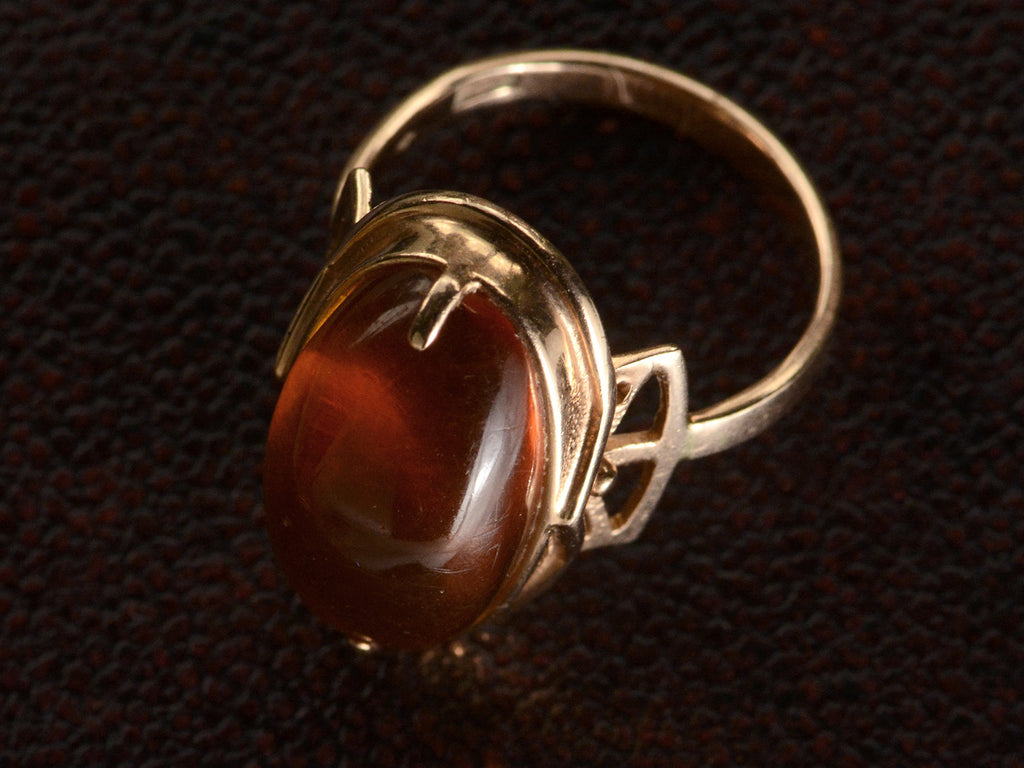 Elevated view vintage ring with an oval amber cabochon in 14k rose gold, shown on dark textured background.