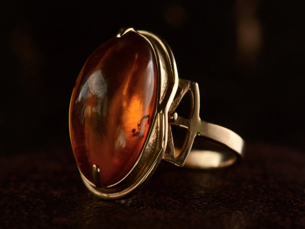 Angled front view of vintage ring with an oval amber cabochon in 14k rose gold, shown on dark background.