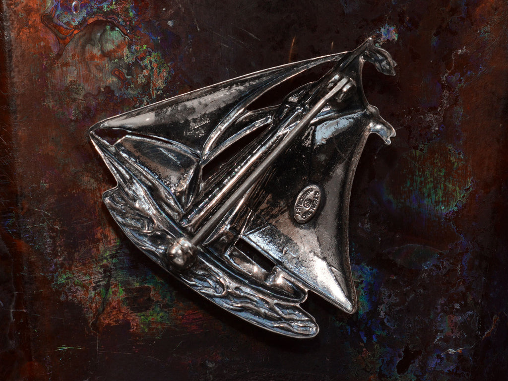 Reverse side of vintage silver sailboat brooch on dark background. A stamp on the inside says "Sterling Danecraft."