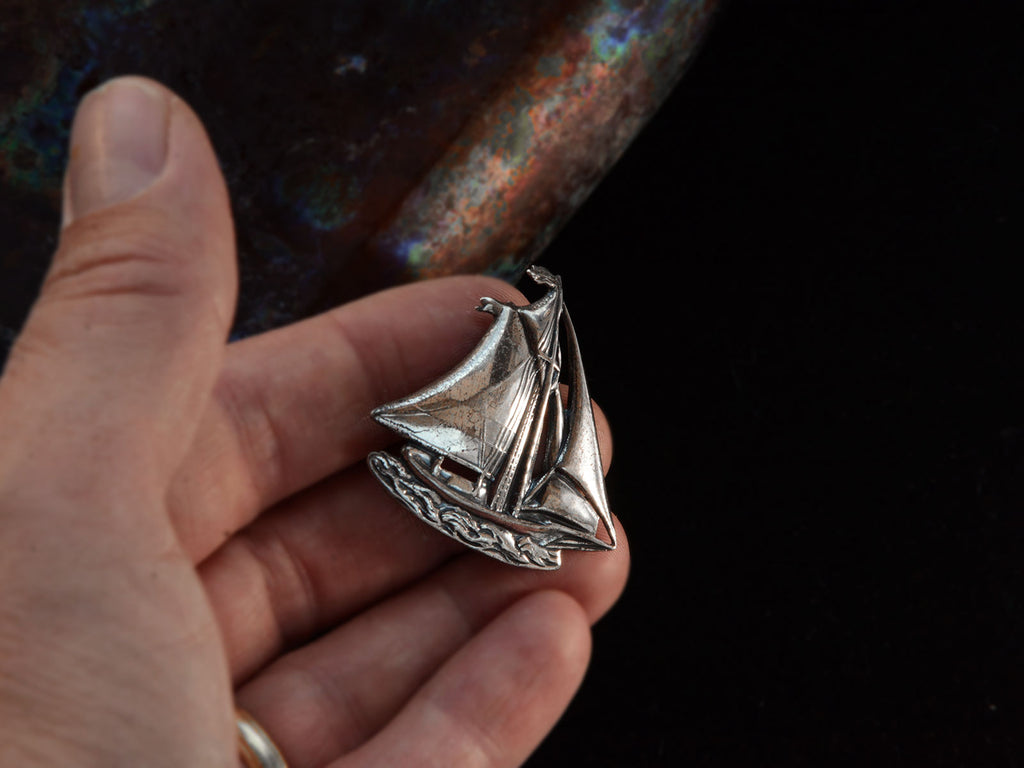 Vintage silver sailboat brooch on hand.
