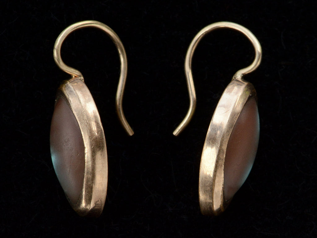 Side profiles of gold earrings with marquise shaped iridescent pale blue saphiret cabochons, shown on black background.