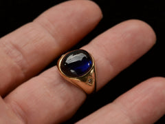 thumbnail of Wide gold antique ring with a large oval blue cabochon and diamonds on the sides, shown on finger.