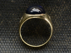 thumbnail of Side profile of wide gold antique ring with a large oval blue cabochon and diamonds on the sides, shown on dark background.