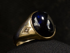 thumbnail of Left side view of wide gold antique ring with a large oval blue cabochon and diamonds on the sides, shown on dark background.