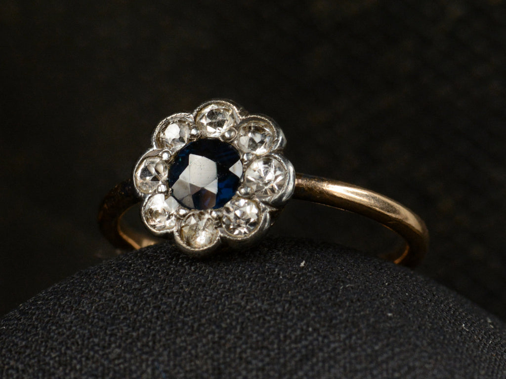 Angled view of antique silver topped gold ring with blue and white sapphires (shown on dark background)