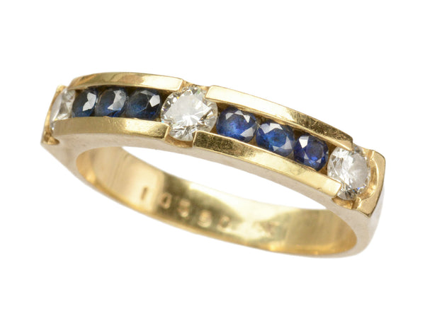Angled view of a vintage yellow gold ring with three diamonds interspersed with blue sapphires. Shown on white background. Faint markings inside the ring read "10590"