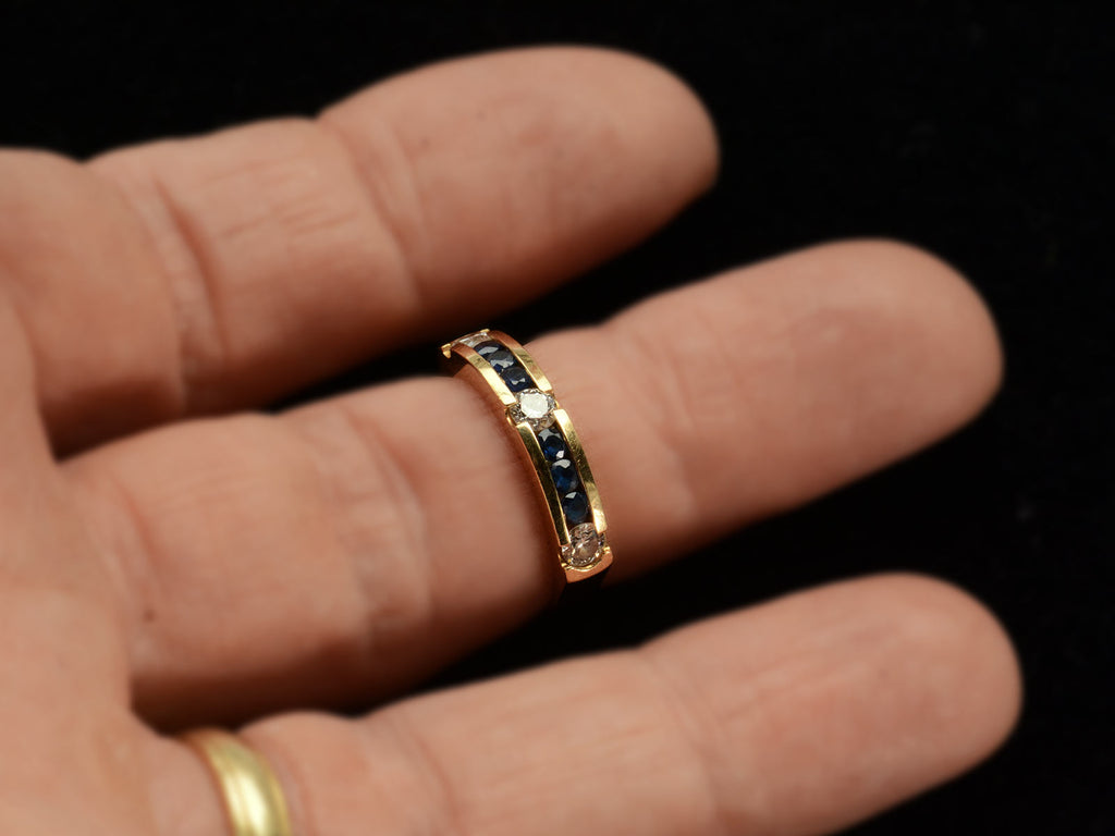 A vintage yellow gold ring with three diamonds interspersed with blue sapphires. Shown on finger.