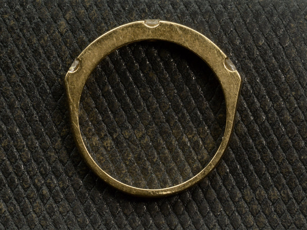 Side profile of a yellow gold ring with three diamonds interspersed with blue sapphires. Shown on dark textured background.