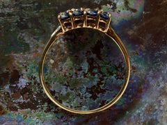 thumbnail of Side profile of a vintage yellow gold ring with a rectangular cluster of blue sapphires, shown on dark textured background.