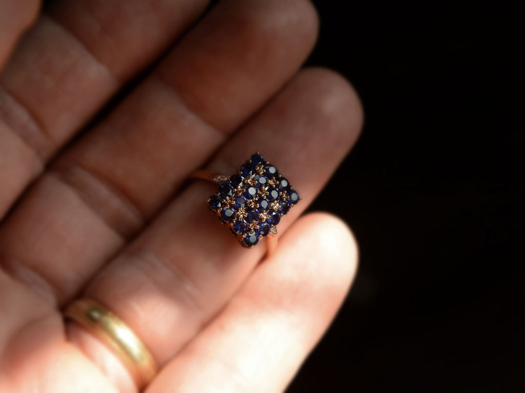 Front view of a vintage yellow gold ring with a rectangular cluster of blue sapphires, shown on hand for scale.