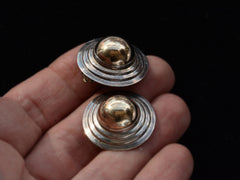 thumbnail of A pair of vintage yellow gold and silver flying saucer shaped earrings on hand.