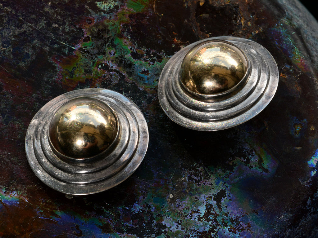 Angled view of pair of vintage yellow gold and silver flying saucer shaped earrings on dark background.