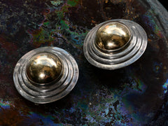 thumbnail of Angled view of pair of vintage yellow gold and silver flying saucer shaped earrings on dark background.